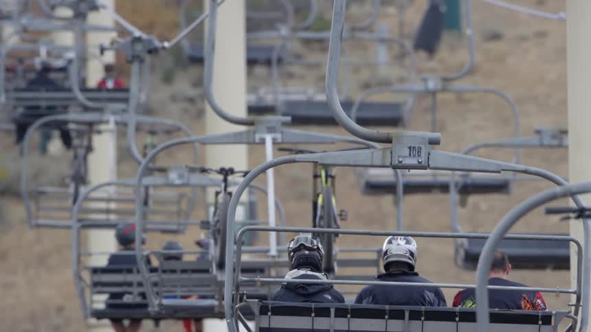 People and bicycles are riding on ski lifts up a hill in daylight