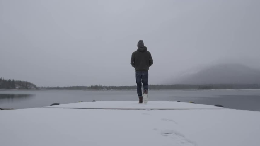 A person slowly walking towards the end of a dock in the winter