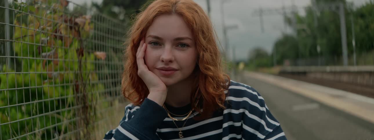 A young woman with reddish brown curly hair wearing a navy and white striped sweater leans her head on her hand