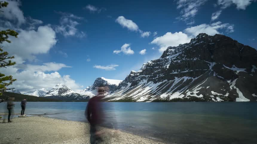 People enjoying the view of a calm lake with snowy mountains in the background