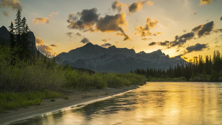 Lake stream next to the shore with forest and mountain region on the background