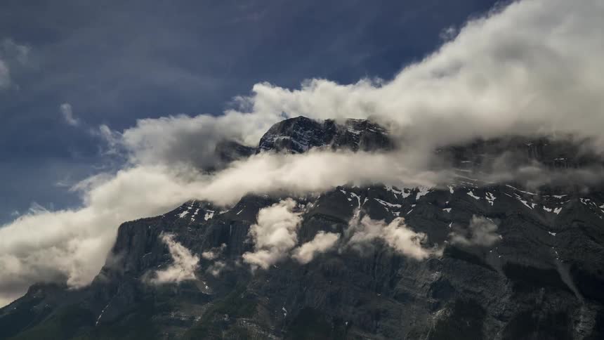 Peak of a rocky mountain with clouds circling around it during day time
