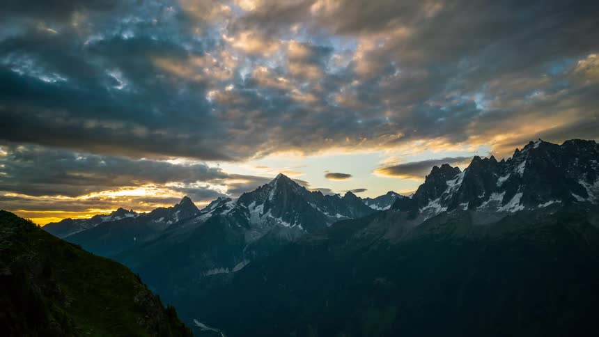 A wide shot of a mountain range at sunrise with a dramatic sky full of clouds and sunlight