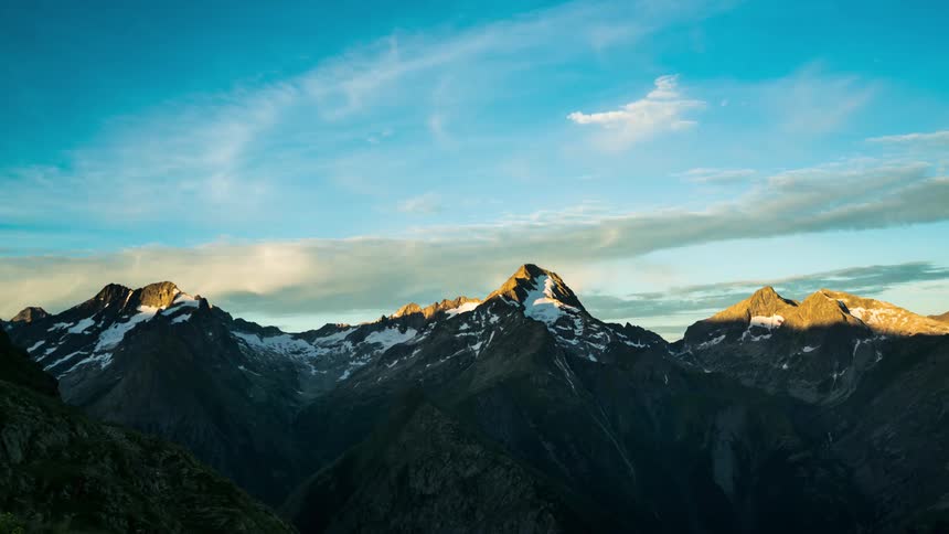 Shadows retreat from mountainous terrain as sunrise becomes daytime under a cloudy sky