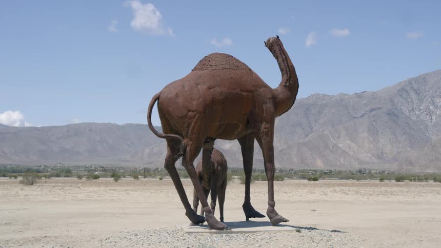 A metal camel sculpture stands in the open desert