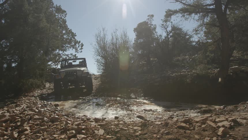 Jeep rolling down through some water along a dirty rocky trail