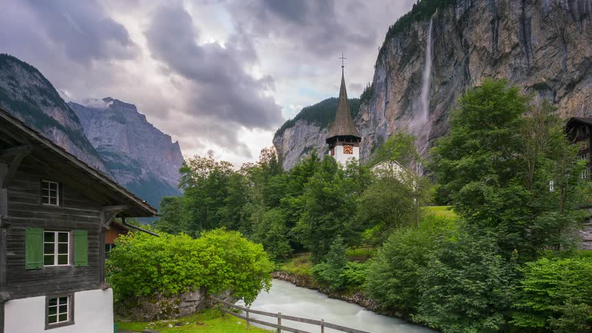 A small town with a church nestled in a mountain valley with a river and waterfall