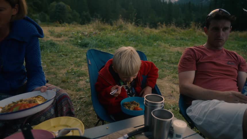A mother and father sit outside with their child sharing a meal in nature