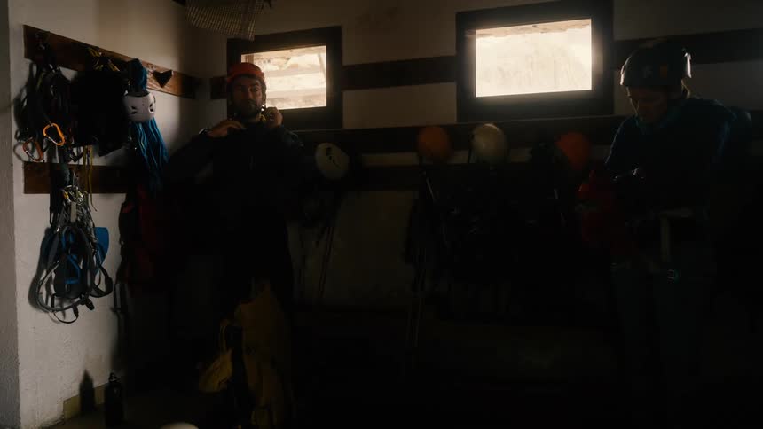 A man and a woman stand in a room putting on mountain climbing gear