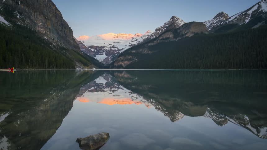 The surface of a lake reflecting the entire environment around it where there are mountains covered in snow and pine forests on the sides