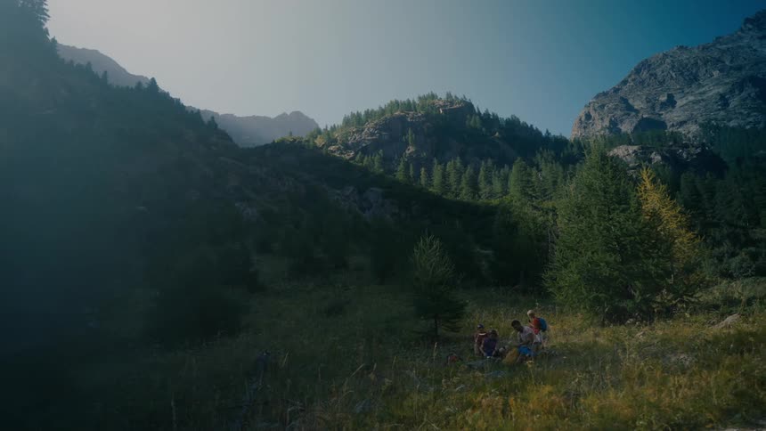 A group of people are having a picnic in a grassy meadow nestled in a mountain valley
