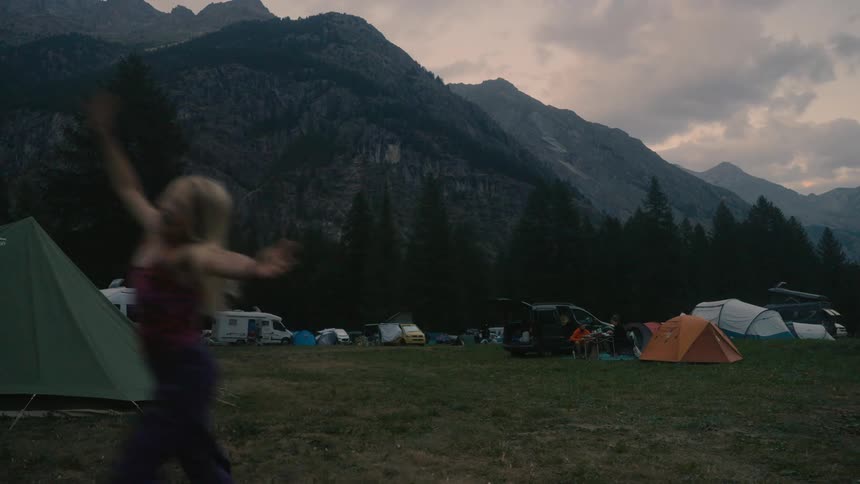 A child jumping and doing a cartwheel while standing in a camping field with tents and mountains in the background