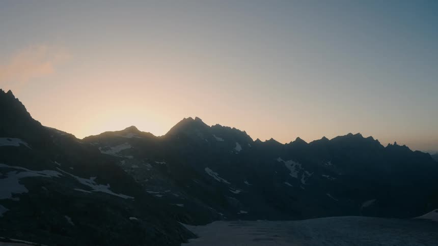 The sun backlights a partially snowy mountain range
