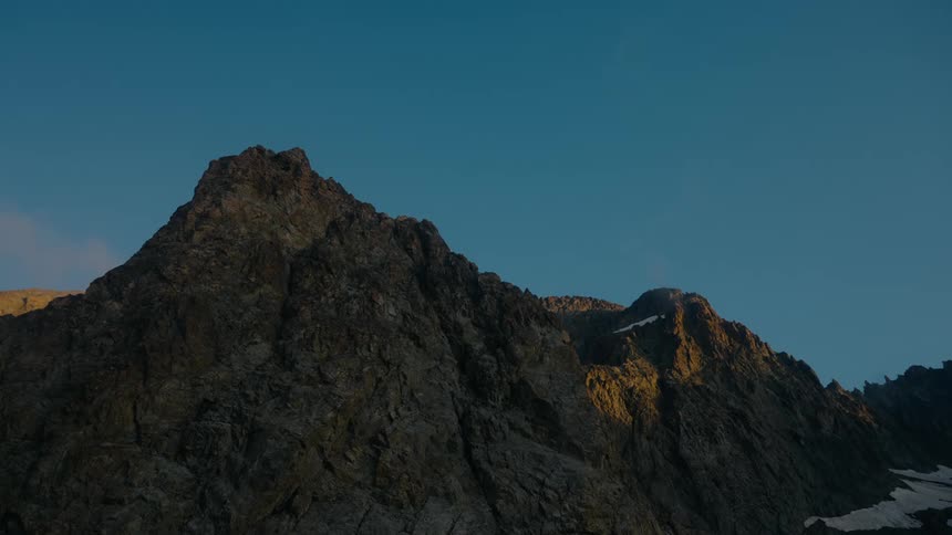 A close up view of rugged dark colored mountain peaks under a clear light blue sky
