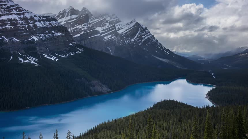 Storm clouds move in over a river next to a partially snowy mountain range