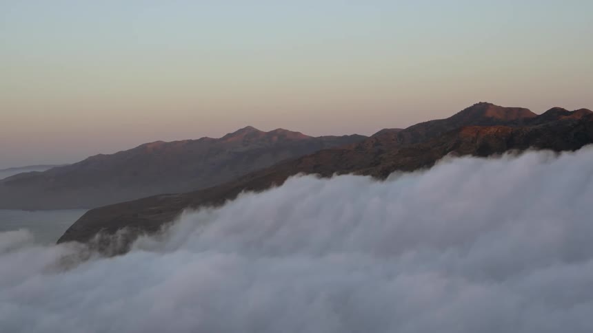 A heavy bank of clouds hovers over mountains and a coastline at dusk