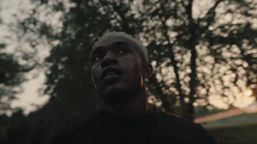 The person sweaty and out of breath is running through a dimly lit forest with the evening light casting shadows around him