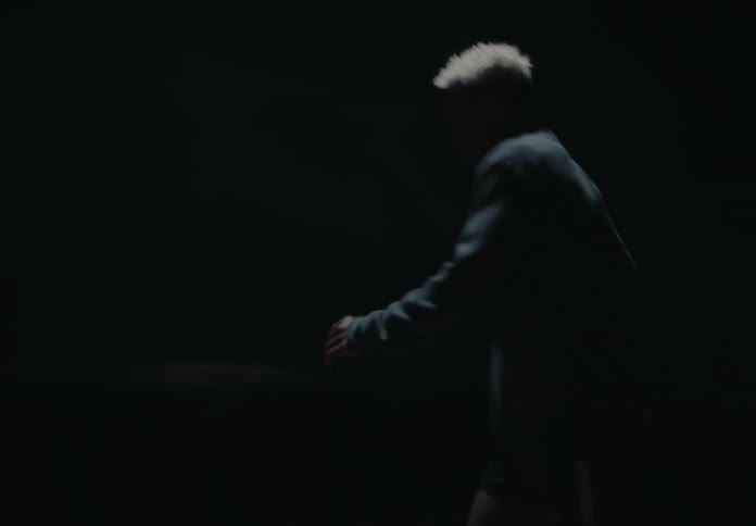 A man is stretching by kicking his legs forward and he is in the middle of a paved street at night