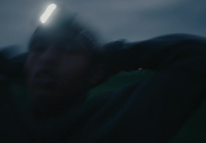 Blurry footage of a young man standing outdoors at dusk with a headlamp