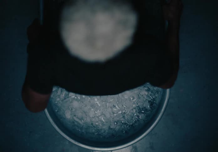 A man is getting into a bathtub that is filled with water with a lot of ice on the surface