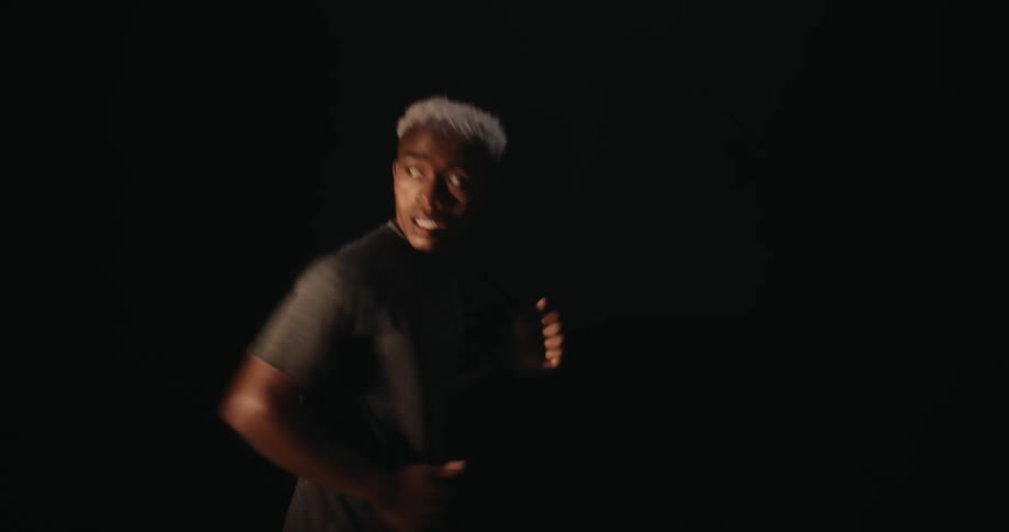 A young man is running at night and then a bright light illuminates his face and he looks back
