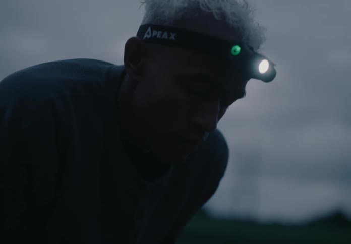 Man in a headlamp rests with his hands on his knees after exercise