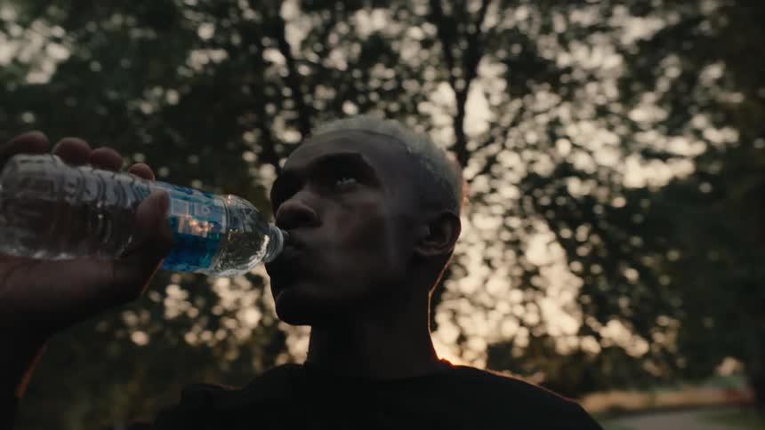 A closeup shot of a man consuming water from a bottle following a morning jog