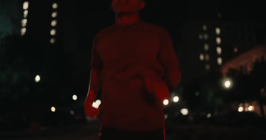 A young man jogs on a city street bathed in red light