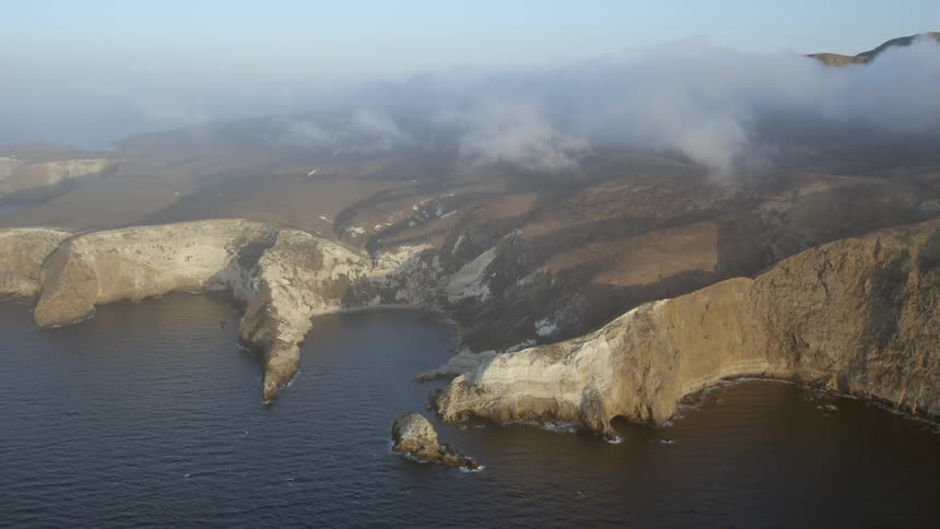 Low clouds are hovering just beyond a rugged coastline during the daytime