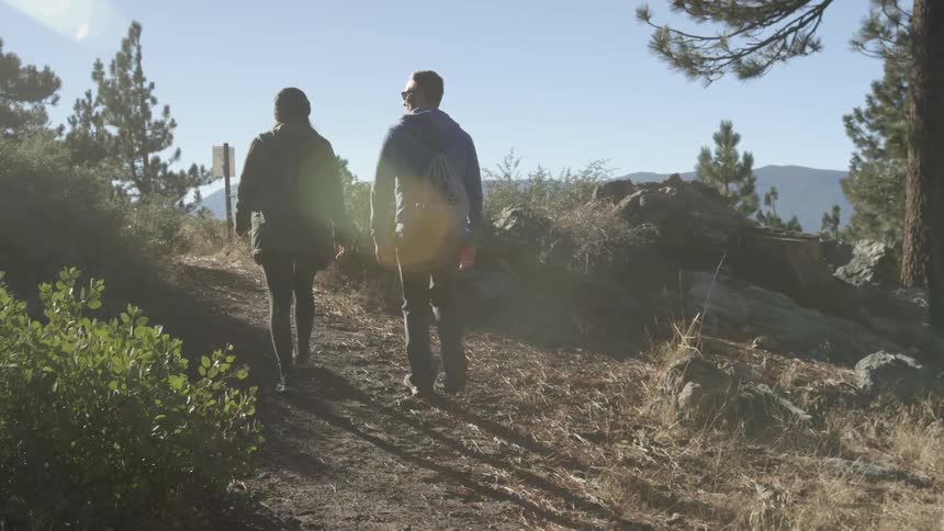Couple hiking a trail towards a sunset on a clear day