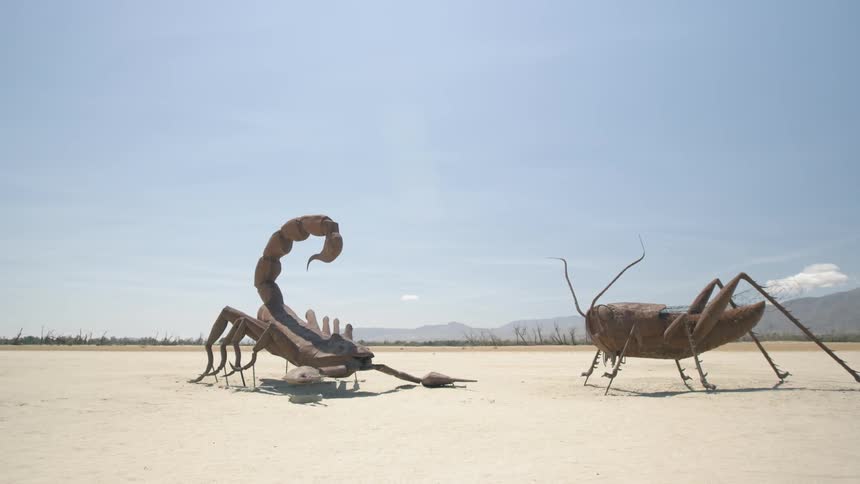 A large scorpion and grasshopper statue stand off in the desert