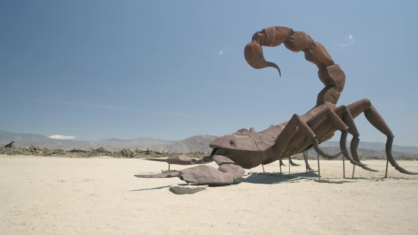 A large metal scorpion stands in the desert on a sunny day