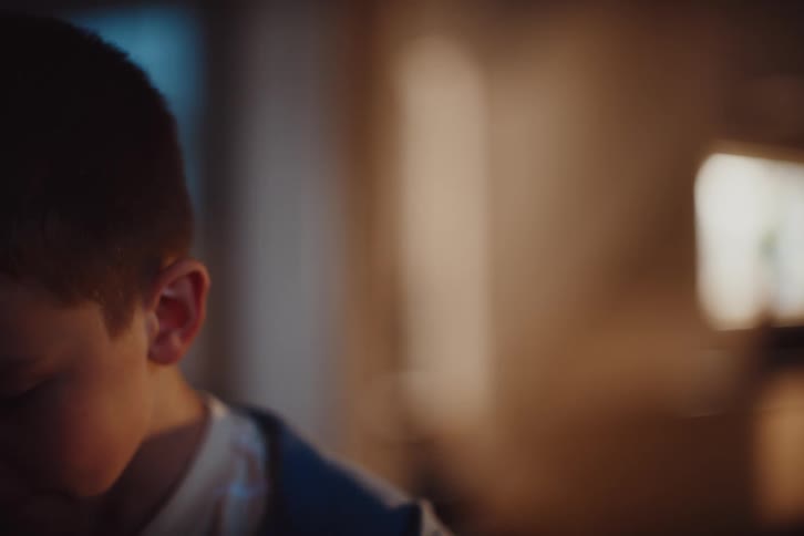 The face of a boy who is looking at something in front of him and he has a subtle smile