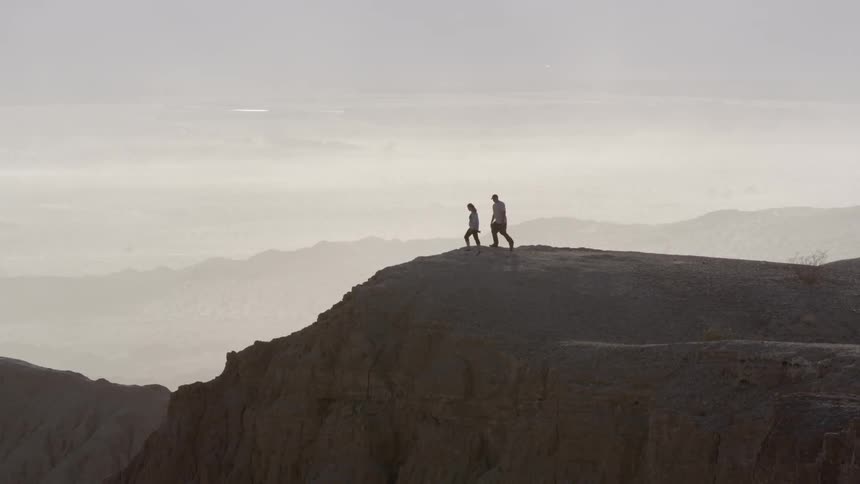A man and woman stand on the top of a rocky hill