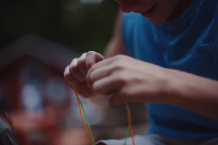 A boy wearing a blue shirt stretching a colorful rubber band