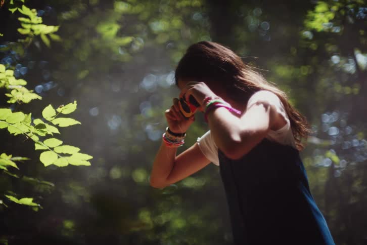 A young girl captures a moment with her camera in a sunlit forest