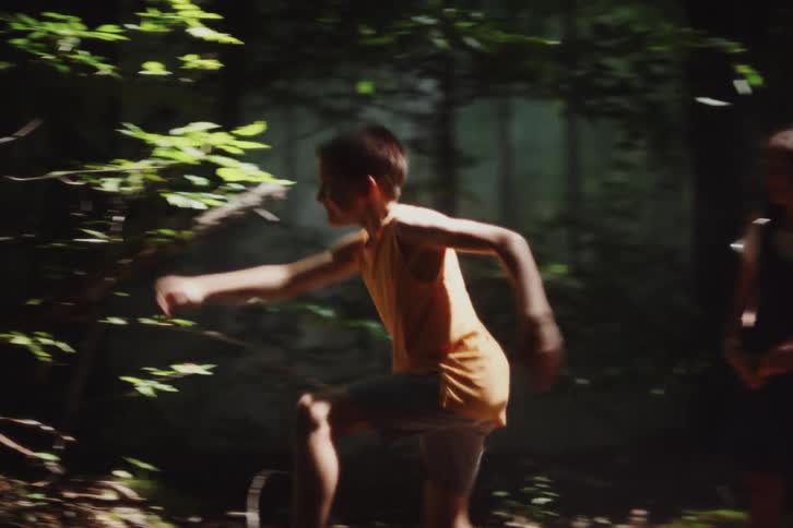 Girl directs playful boy to pose near trees so she can take a picture during a day in the woods