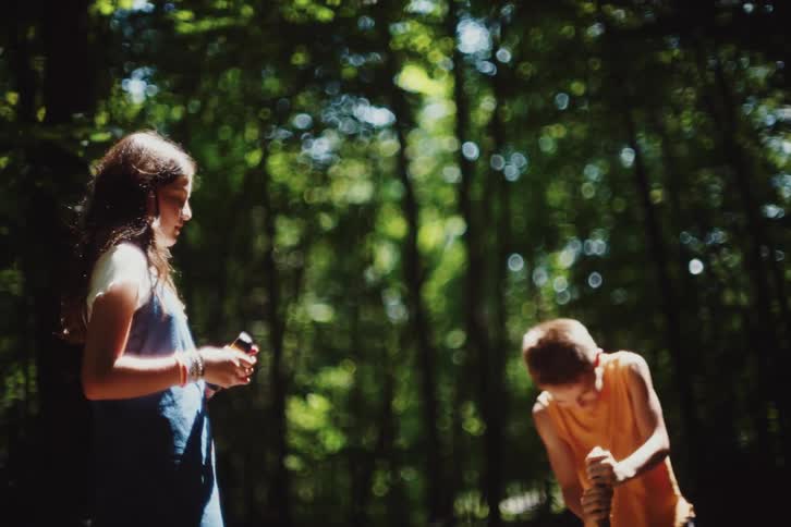 Boy spinning with a wooden log in a forest playing and a girl watching