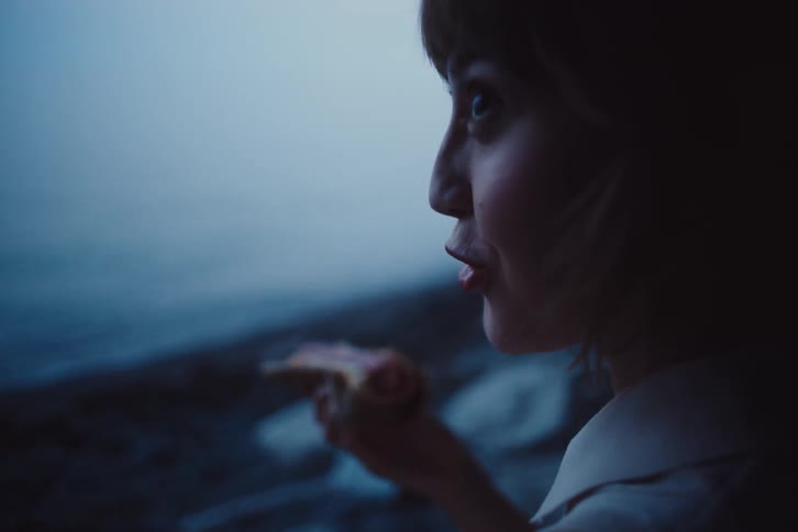 The face of a young woman who is talking to someone who is next to her and she greets the person with her hot dog