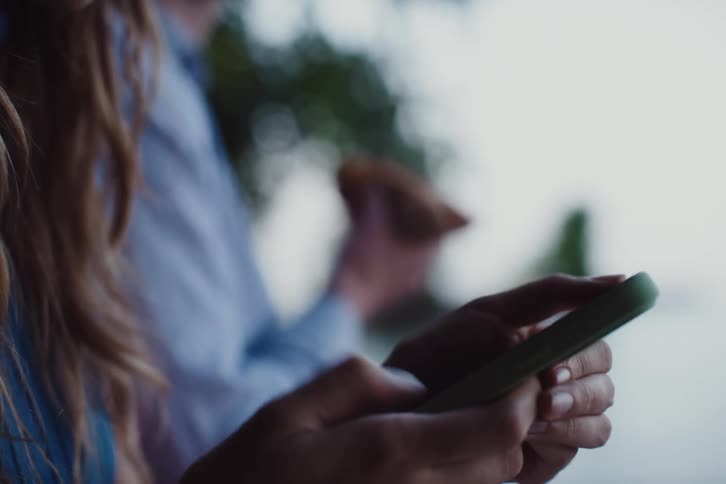 Woman typing on an iphone and a man standing next to her