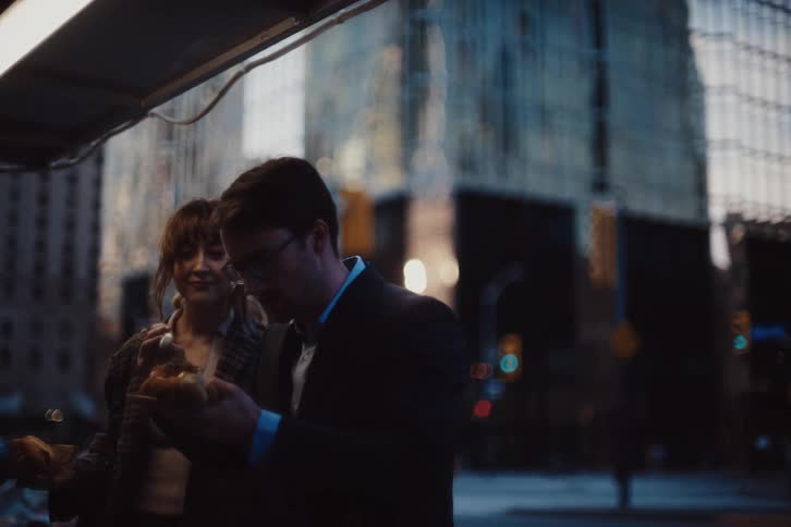 A man and a woman are talking while putting something on their hot dogs that are in their hands