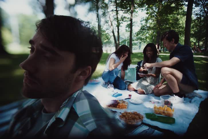 Man sadly sits apart from his friends during a birthday picnic in the park