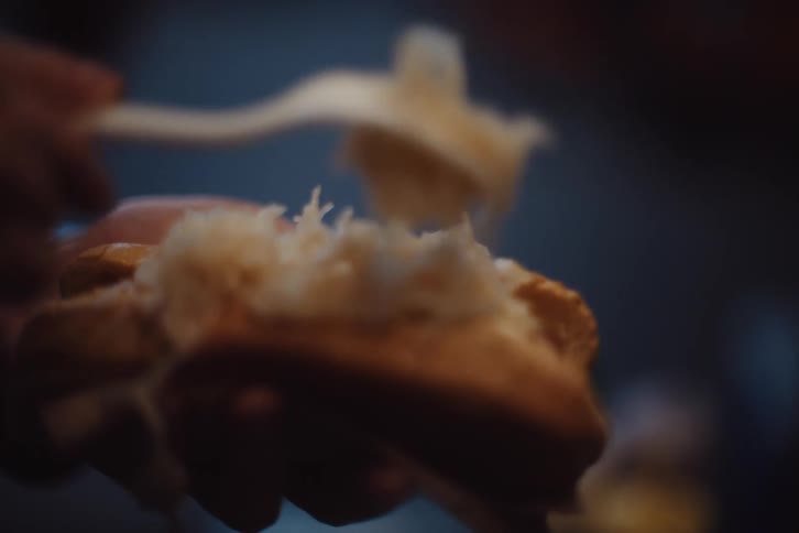 Toppings are being put on the hot dog with a fork