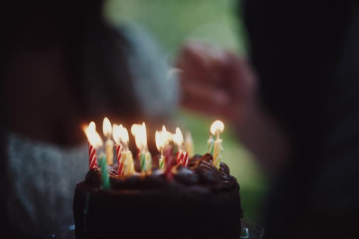 Persons hand finishing lighting candles on a chocolate birthday cake