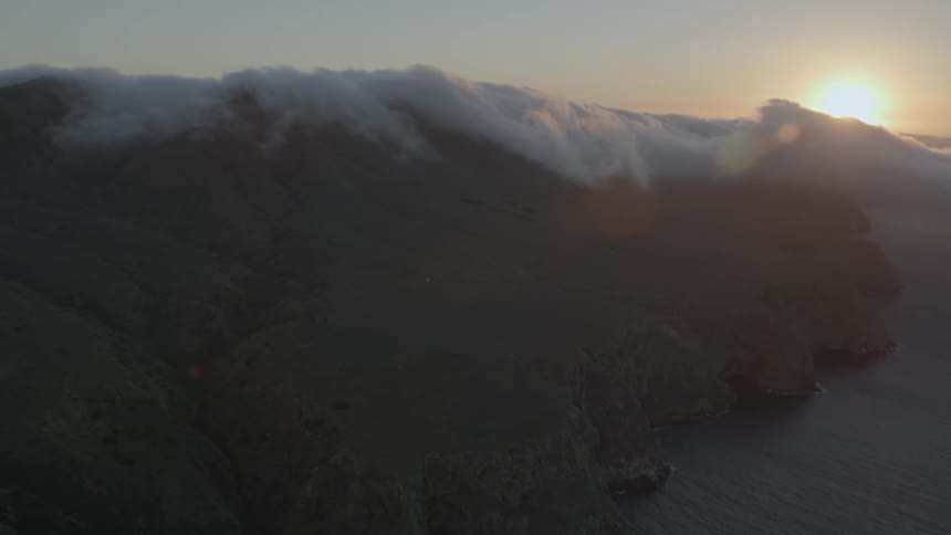 Sun setting behind a cloud covered mountain