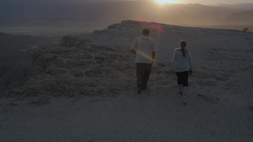 A man and woman are walking along a canyon edge at sunset