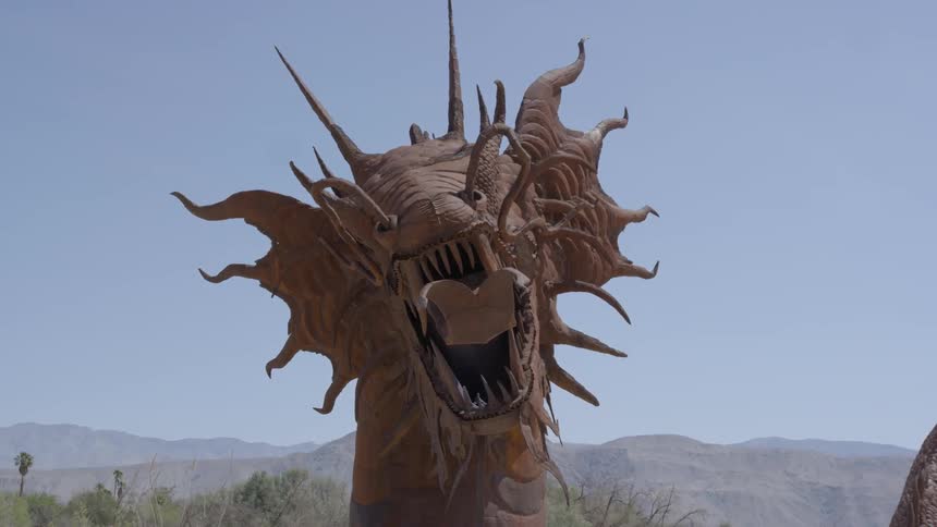 A massive brown and very detailed dragon sculpture outside surrounded by mountains