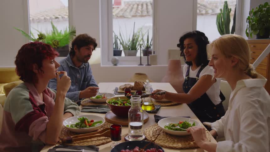 Man and three women sitting at a table with salad and spices eating and talking