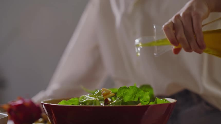 A woman drizzles olive oil over a homemade salad