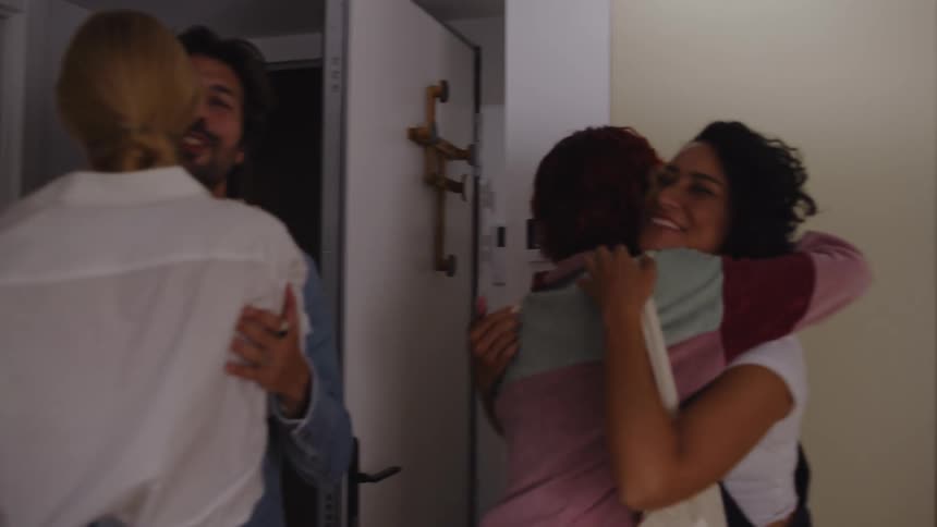 Woman opening the door and friends come in and greet each other happily